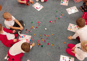 Dzieci siedzą na dywanie – grają w „Bingo – symbole narodowe”.